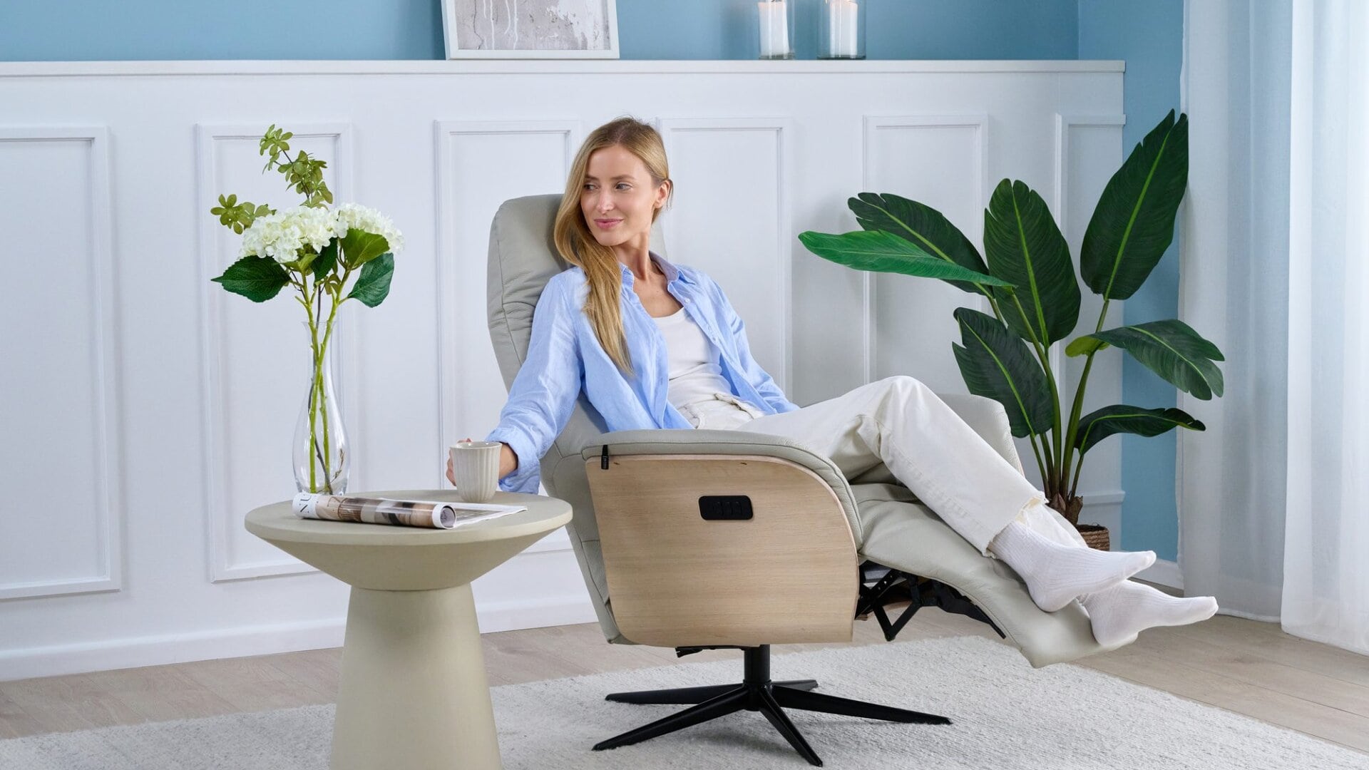 Skagen Studio Hejrede Essential recliner in Madras white leather, reclined with the footrest out, a woman relaxing with a cup of coffee.