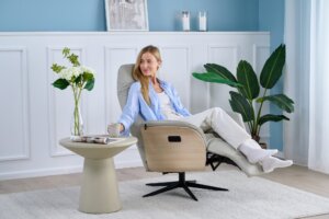 Skagen Studio Hejrede Essential recliner in Madras white leather, reclined with the footrest out, a woman relaxing with a cup of coffee.